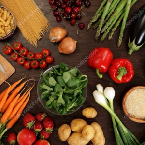 מגוון ירקות ופירות כגון גזרים, עלים, פלפלים, עגבניות שרי, דובדבנים ותות-שדה. מונחים על שולחן בצבע חום