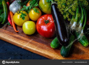 מגוון ירקות כמו חציל, עגבניות, מלפפוןנים ובצל ירוק. מצולמים מקרוב על קרש חיתוך במבט מקרוב