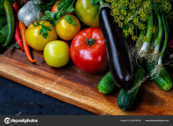 מגוון ירקות כמו חציל, עגבניות, מלפפוןנים ובצל ירוק. מצולמים מקרוב על קרש חיתוך במבט מקרוב