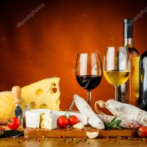 בקבוק יין אדום ובקבוק יין לבן עם כוסות יין ומגוון גבינות המונחות על השולחן ברקע חום.
