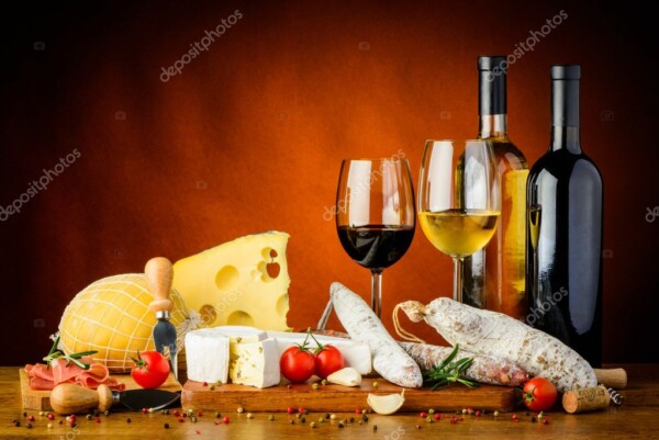 בקבוק יין אדום ובקבוק יין לבן עם כוסות יין ומגוון גבינות המונחות על השולחן ברקע חום.