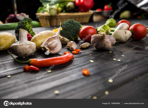 מגוון ירקות כמו שום, עגבניה וברוקולי. מפוזרים על שולחן מעץ ברקע כהה במבט מהצד.
