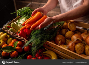 מוכר מגיש גזרים מעל דוכן ירקות עם ארגזים וסלסילות של ירקות
