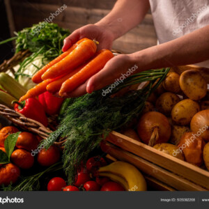 מוכר מגיש גזרים מעל דוכן ירקות עם ארגזים וסלסילות של ירקות
