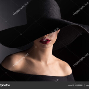 אישה בצילום מגובה כתפיים עם כובע שחור רחב שוליים ואודם אדום_141009944