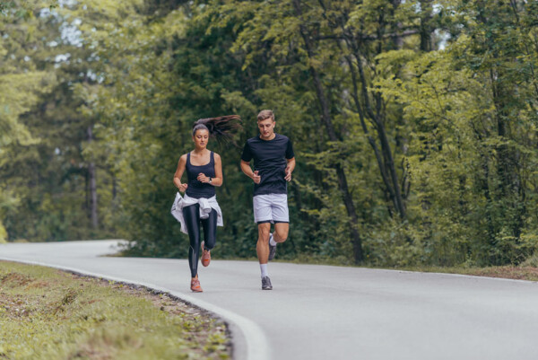 גבר ואישה רצים בדרך אספלט בתוך יער - תמונת טבע - תמונת ספורט - צלם gorgev_413913194